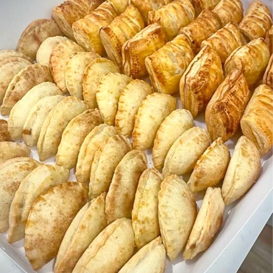 several rows of empanadas and pastelitos in a white tray